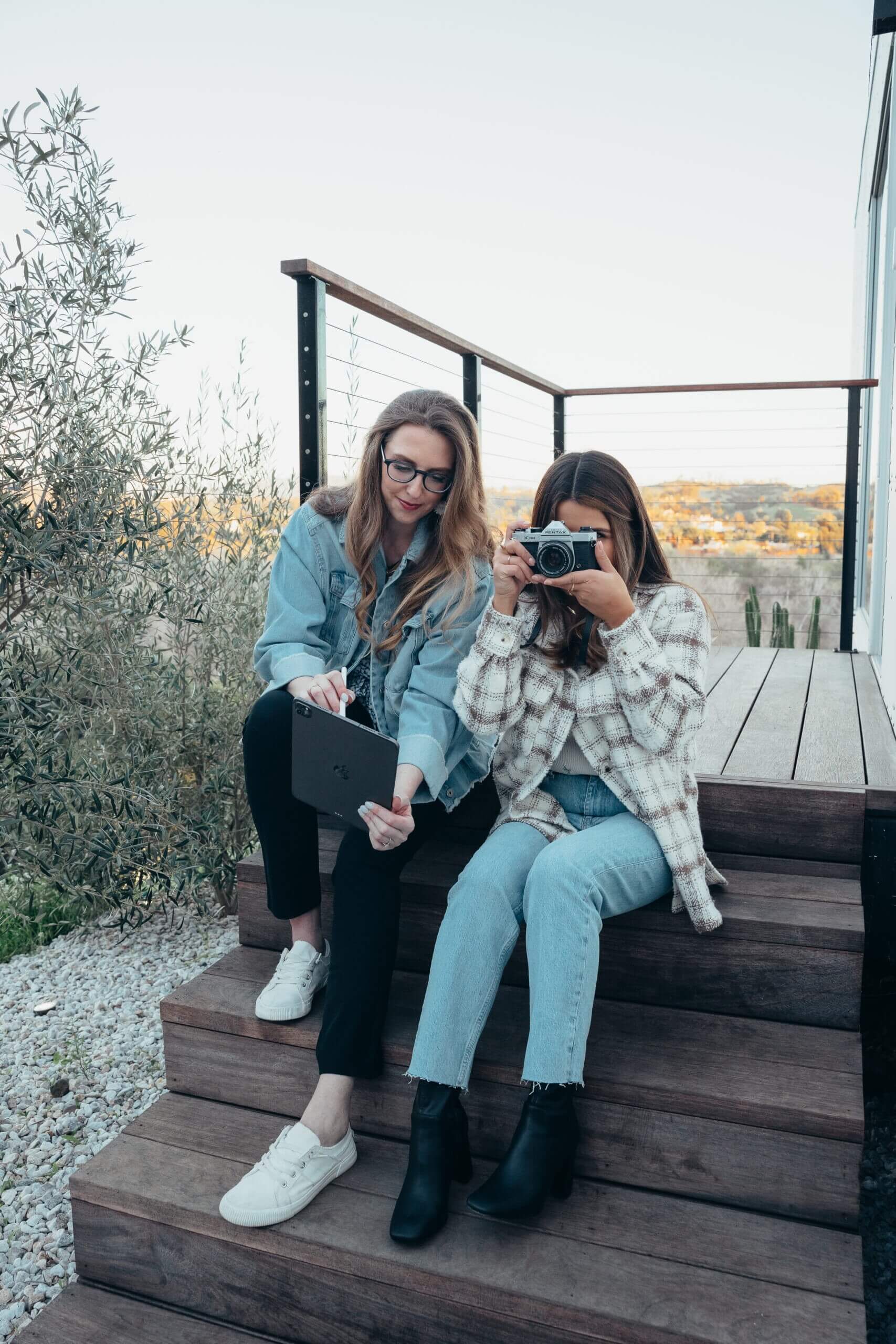 two women sitting on a staircase one is using a tablet and one is taking a photo