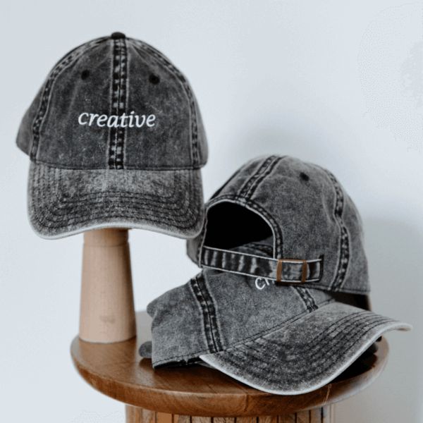 Grey embroidered hat with the word "Creative" showing the back side buckle