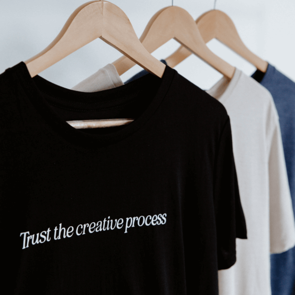 3 shirts hanging from hangers with "Trust the creative process" written on the chest