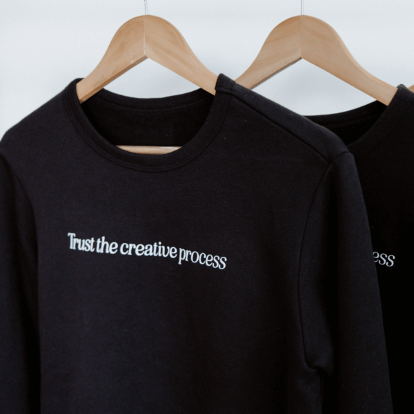 Black shirts hanging with "Trust the creative process" written on the chest