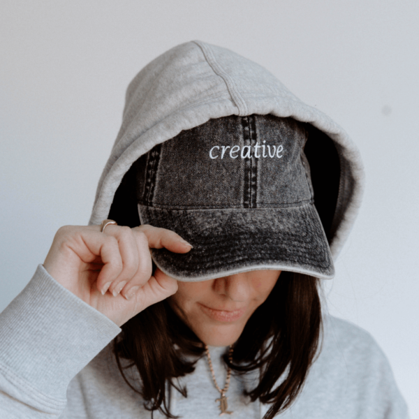 girl looking down wearing a cap with the word "Creative" embroidered on it
