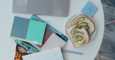desk with laptop and other desk accessories and a plate with avocado toast