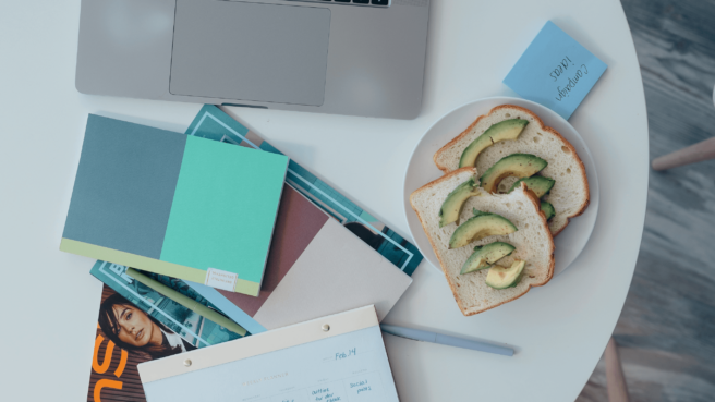 desk with laptop and other desk accessories and a plate with avocado toast